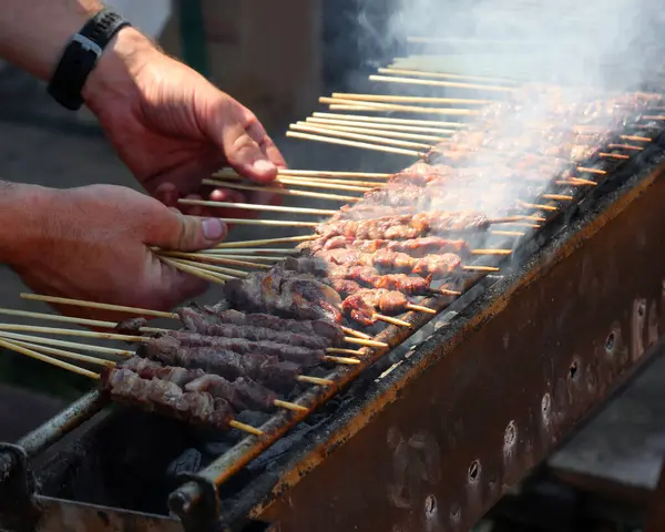 stock image hand of the chef who turns the meat skewers called ARROSTICINI cooked on the burning embers typical of the cuisine of Southern Central Italy in the Abbruzzo and Molise regions