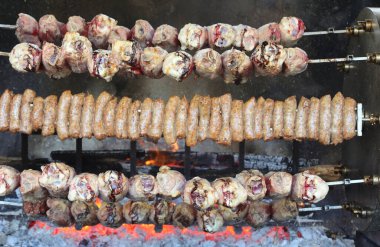 Köy festivali sırasında yanan közlerin üzerinde dönen et ve sosis şişleri ile büyük bir rosto.
