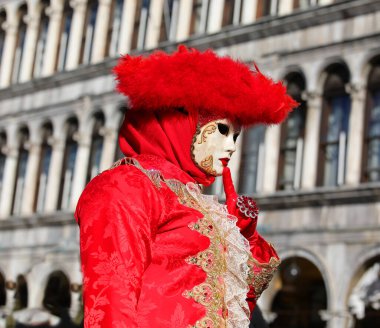 Kuzey İtalya 'daki Venedik Karnavalı sırasında yüzünde kırmızı elbise ve başlık ve arka planda antik bir saray olan maskeli adam.