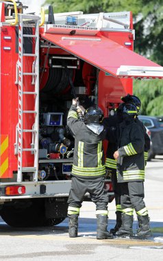 Üniformalı ve koruyucu giysili itfaiyeciler yangını söndürmek için itfaiye arabalarından su hortumunu çıkarıyorlar.