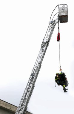 Korkusuz itfaiyeci, yaralıyla birlikte boşluğa bağlı bir sedyeyle itfaiye arabasının merdivenine asılmış.