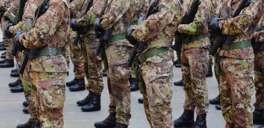 Yeşil ve kahverengi kamuflaj üniformalı, siyah eldivenli ve tüfekli bir sürü asker.