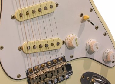 Ses, ton düğmeleri ve pikapları olan fildişinden beyaz bir elektro gitarın yakın plan görüntüsü.