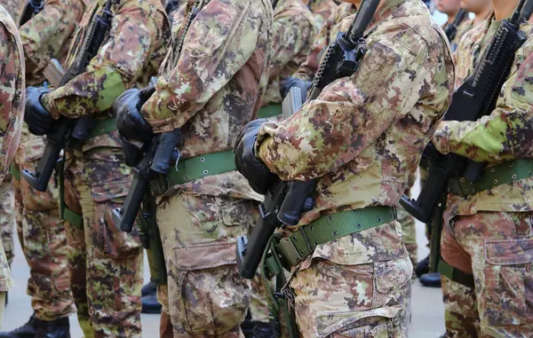Yeşil ve kahverengi kamuflaj üniformalı, siyah eldivenli ve tüfekli bir sürü asker.