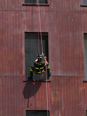 Kışladaki tatbikat sırasında miğferli ve üniformalı itfaiyeciler binadan iple iniyor.