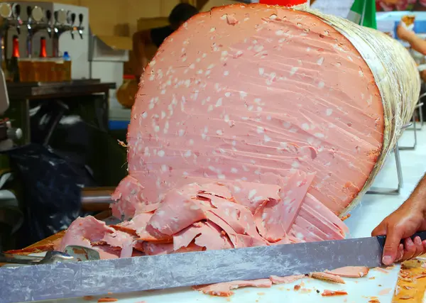 stock image chef with a very long knife slicing a gigantic sausage called MORTADELLA in Italy