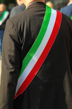 Siyah ceketli zarif İtalyan belediye başkanı ve geçit töreni sırasında İtalyan bayrağının üç renkli kuşağı.