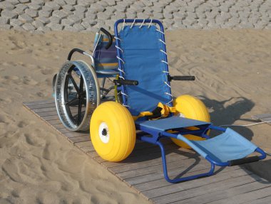 Plaj tekerlekli sandalyesi suya giriyor sarı şişirilebilir ve yüzen tekerleklerle ve plajda hareket etmek için metal tekerlekleri olan başka bir tekerlekli sandalyeyle.