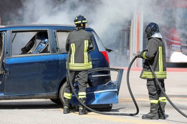 Kasklı iki cesur itfaiyeci, araba kazasından sonra caddedeki yangın musluğuyla çıkan yangını söndürdü.