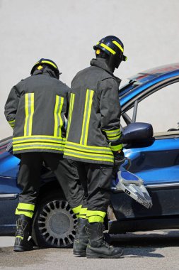 team of firefighters using powerful hydraulic shears and spreaders open the doors of the car after the road accident to free injured victims clipart