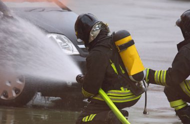 fireman with mask and oxygen tank spraying extinguishing foam on the damaged car after the accident clipart