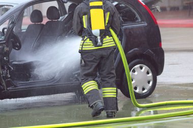 Maskeli ve oksijen tüplü itfaiyeci kazadan sonra hasarlı arabaya köpük püskürtüyor.
