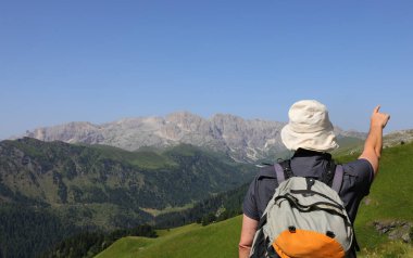 Yazın dağları gösteren şapkalı ve sırt çantalı bir yürüyüşçü.