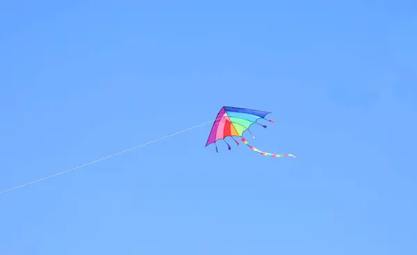 stock image kite with rainbow colors flying in the blue sky tied to a string