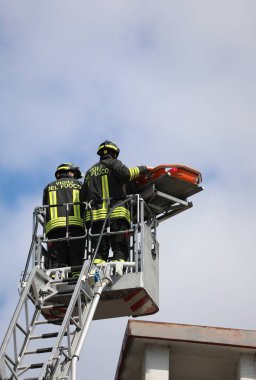 Vicenza, VI, İtalya - 23 Mayıs 2024: Çatıdaki yaralı adamın kurtarılması sırasında sedyeyle sedye taşıyan İtalyan itfaiyeciler