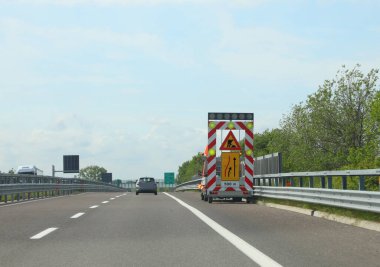 Yol bakımını ve otoyol şeridini daraltmayı gösteren dev bir işaret levhası olan işçiler minibüsü.