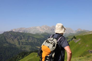Sırt çantalı ve şapkalı genç yürüyüşçü yazın İtalya Alp Dağları 'nda yürüyüş yaparken.