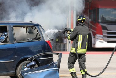 İtfaiyeci kazadan sonra araba yangınını söndürmek için su ve yangın söndürücü sıkar.