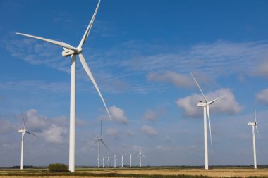 many wind turbines on the plain in the middle of the cultivated field for the production of electricity from renewable sources without polluting and without CO2 emissions into the air clipart