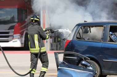 İtfaiyeci kazadan sonra araba yangınını söndürmek için su ve yangın söndürücü sıkar.