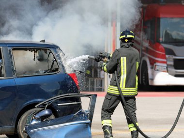 Kasklı ve üniformalı cesur itfaiyeci araba kazasından sonra çıkan yangını söndürdü.