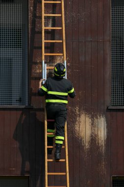 İdman sırasında kask takan üniformalı itfaiyeci merdivenlere tırmanıyor.