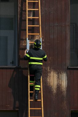 Firefighter in uniform with portective helmet climbing ladder during training clipart