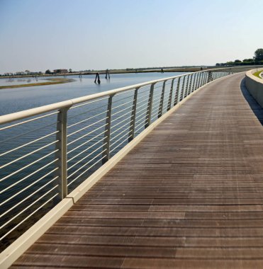 new cycle path made of wood and steel railings that runs along the Venetian lagoon at Treporti near Jesolo and the island of Venice without bikes in summer clipart