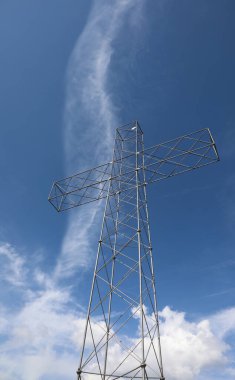 Mavi gökyüzü olan bir dağın tepesinde çok büyük metalik bir haç