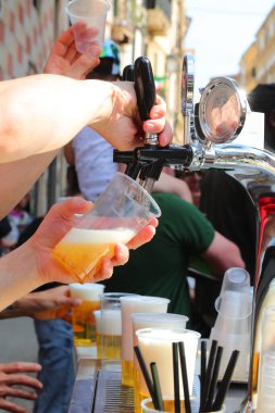 Gündüz vakti açık hava köyü festivalinde bardağa buz gibi sarışın birası dolduran barmenin eli.