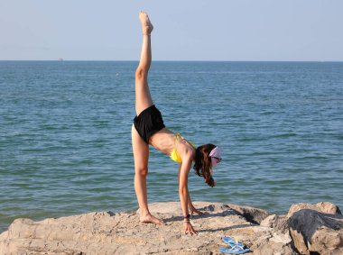 Bir bacağı çok yüksek kayaların üzerinde dengede duran genç kızlar ve diğeri 180 derecelik bir açı oluşturuyor.