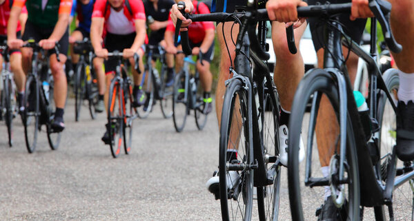 много велосипедистов с педалями во время велогонки по асфальтированной дороге с неузнаваемыми лицами