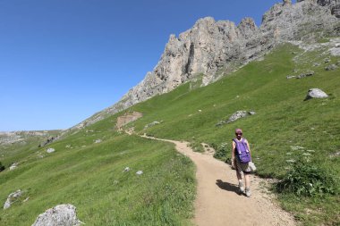 Genç kadın yürüyüşçü yalnız başına yazın sırtında sırt çantasıyla İtalyan Alpleri 'nde Dolomitlerin patikasında yürüyor.