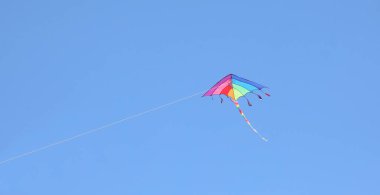 Mavi gökyüzündeki birçok renk gibi tek başına uçan uçurtma ve onu çocukluk ve aydınlığın sembolü olarak tutan ip.