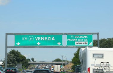 Kuzey İtalya 'da bir otoyol kavşağında yoğun trafik var. Venedik Bologna ve havaalanı gibi yerleri gösteren işaretler var.