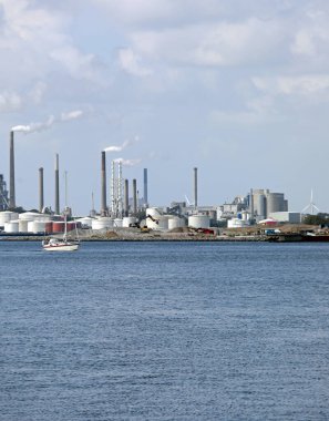 Üretim sırasında beyaz duman ve deniz kıyısı püskürten bacaları olan büyük bir çimento fabrikası.