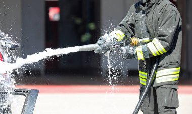 Üniformalı itfaiyeci acil bir durumda yangına köpük püskürtmek için hortum kullanıyor.