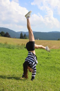 agile athletic girl performs a cartwheel with her legs high up in the air on the green mountain meadow symbolizing happiness joy and carefree bliss clipart