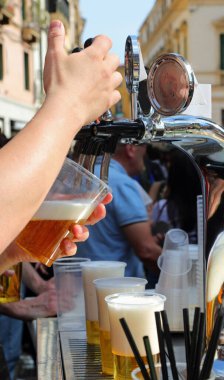 Gündüz vakti açık hava köyü festivali sırasında bardakta çok taze bira yudumlayan barmenin eli.