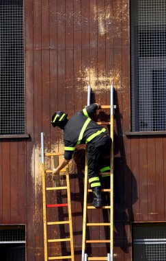 Üniformalı ve miğferli itfaiyeci, itfaiye istasyonundaki tatbikat sırasında merdiven kuruyor.