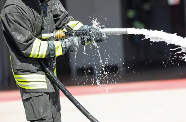 Acil durum sırasında yangın söndürmek için beyaz köpük püskürten bir hortumla üniformalı itfaiyeci.