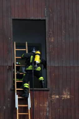İtfaiye istasyonunda tahta merdiven kullanarak pencereye giren oksijen tüplü bir itfaiyeci.