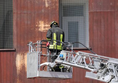 İtfaiye istasyonundaki tatbikat sırasında üniformalı itfaiyeci metal sepetin içinde merdivenin üzerinde duruyor.