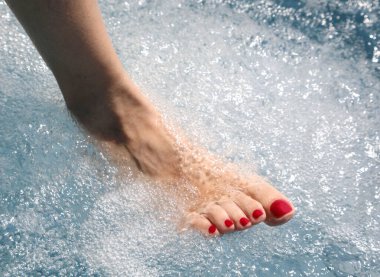 Manikürlü, parlak kırmızı tırnak cilası olan kadın, kan dolaşımını iyileştirmek ve rahatlamak için sıcak bir ayak banyosu yapıyor.