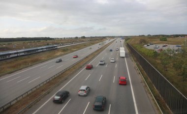 Dört şeritli otoban üzerinde arabalar ve araçlar düz yolda hızla ilerlerken yukarıdan görülüyor.