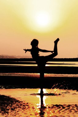 Sahilde bacağını geriye doğru tekmeleyen genç bir kız silueti. Ufukta güneş vardı.