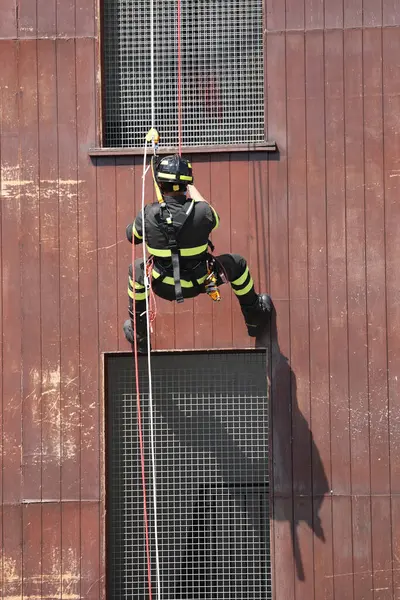 Cesur itfaiyeci acil bir durum sırasında kask ve üniforma giymiş bir halatla binadan iniyor.