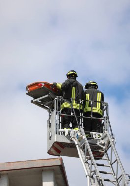 Kurtarma operasyonu sırasında sepetinde metal yapıya bağlı sedyede yaralı bir adamı taşıyan iki itfaiyeci var.
