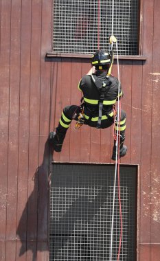 Cesur itfaiyeci üniformalı ve kasklı bir şekilde binadan aşağı iple iniyor.