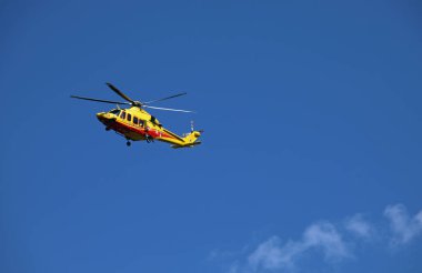 Trento,TN, Italy - July 30, 2024: Yellow helicopter of Italian firefighters flying high in the sky during an emergency to reach the injured and transport them to the hospital clipart